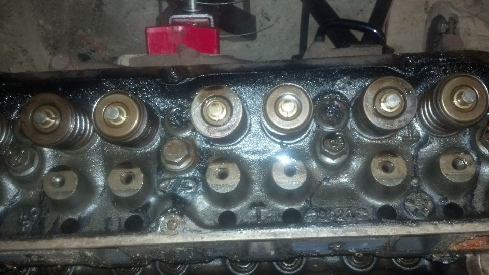 Close-up of Ford V8 cylinder head with valve springs and retainers, covered in oil.