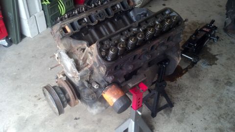 1988 Ford Bronco - A V8 engine block with valve covers removed sits on jack stands in a garage setting. A hydraulic jack and various tools are visible around…