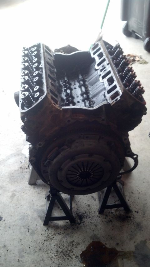 1988 Ford Bronco - A disassembled V8 engine is mounted on jack stands in a garage setting. The engine block, cylinder heads, and clutch assembly are visible,…