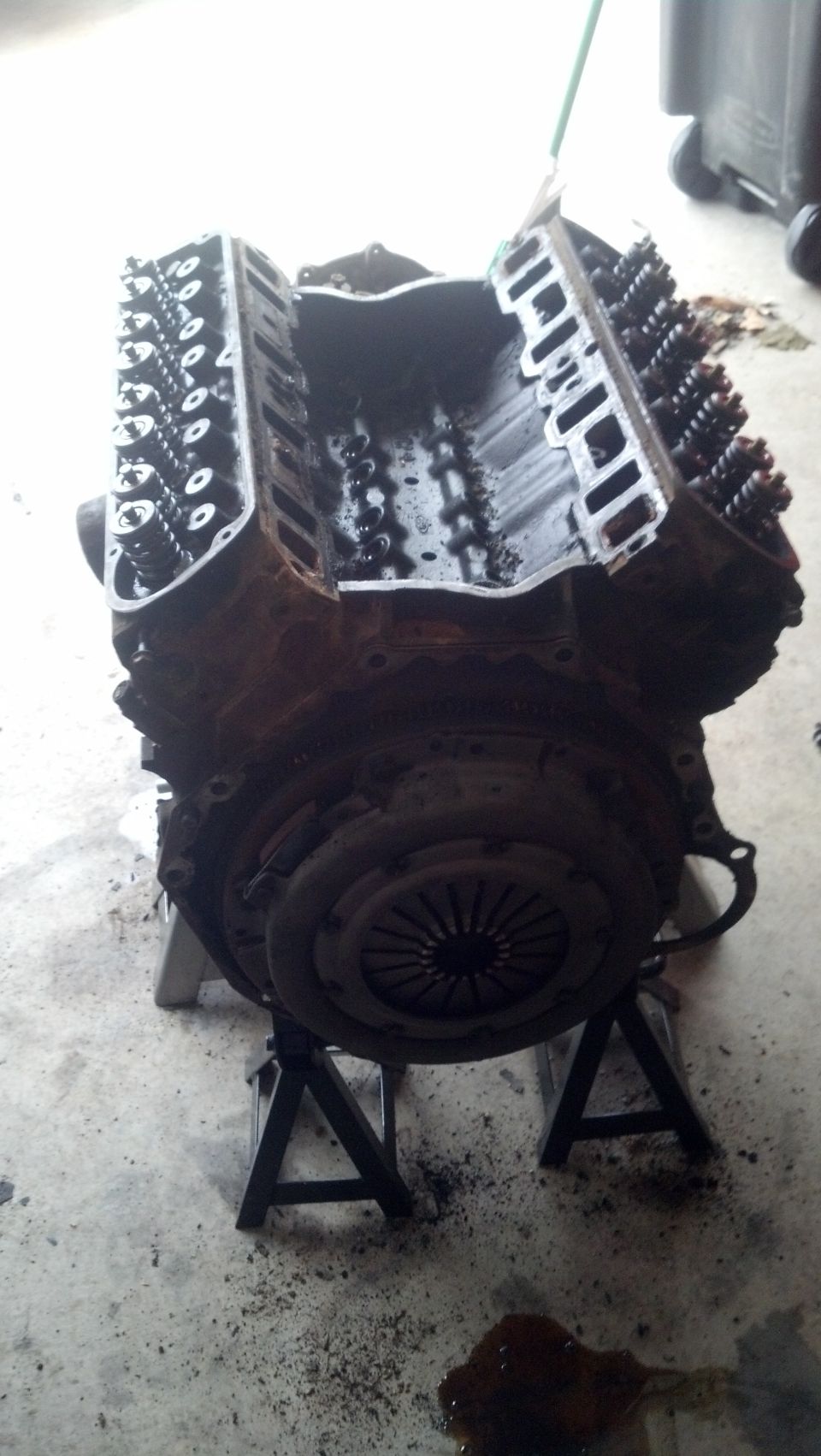 Disassembled V8 engine on jack stands, showing engine block, cylinder heads, and clutch.