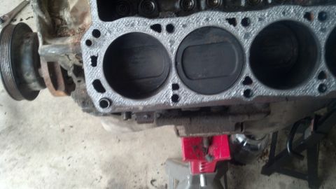 1988 Ford Bronco - Close-up view of the cylinder block of a V8 engine, showing two pistons within their cylinders. The engine block is supported by a red jack…
