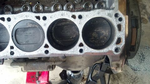 1988 Ford Bronco - A close-up, overhead view of the cylinders and pistons of a V8 engine block. The engine block is heavily soiled and appears to be undergoin…
