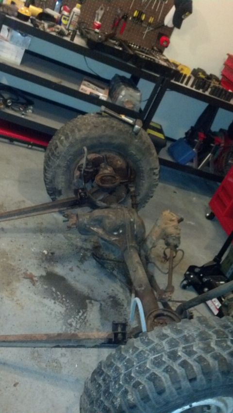 1988 Ford Bronco - A disassembled front axle assembly with a tire attached is on the floor of a garage or workshop. The axle appears to be rusty and is positi…