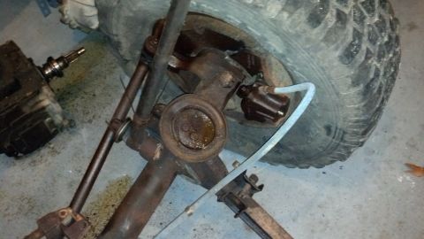 1988 Ford Bronco - Close-up view of the front axle, steering components, and brake assembly of a vehicle.