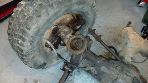 1988 Ford Bronco - Close-up of a vehicle's front axle assembly and tire, with visible rust and grease.