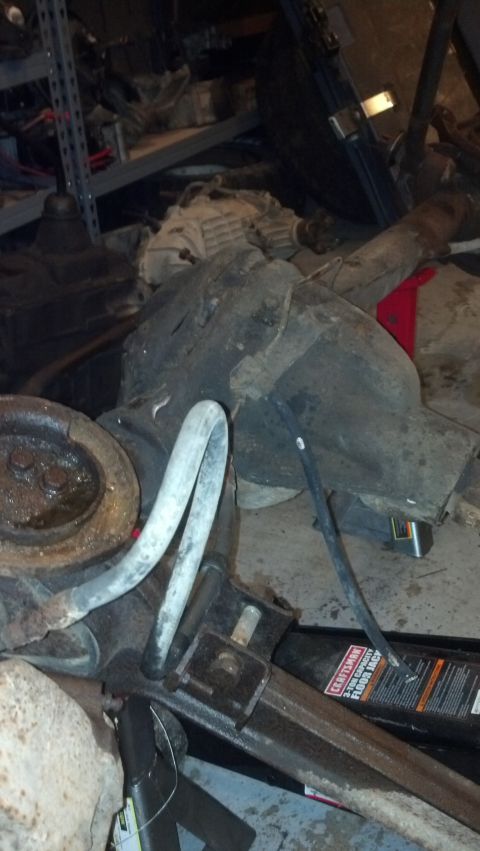 1988 Ford Bronco - Various vehicle parts, including an axle and differential, are stored on the floor with a jack.