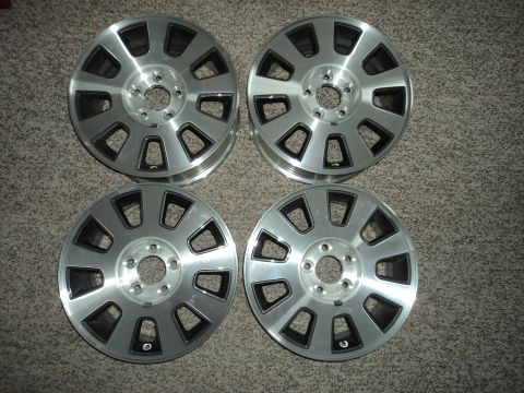 2004 Mercury Grand Marquis - Four aluminum alloy wheels with a silver finish and black accents are laid out on a carpeted surface. Each wheel has ten spokes with cutout…