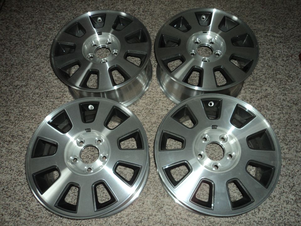 Four silver alloy wheels with black accents on a carpeted floor.