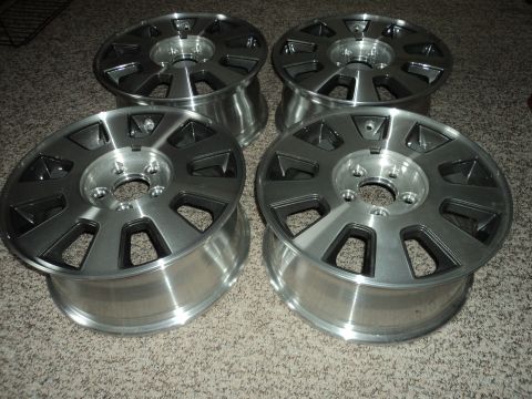 2004 Mercury Grand Marquis - Four silver alloy wheels with black accents are displayed on a carpeted floor. The wheels have a multi-spoke design with triangular cutouts.