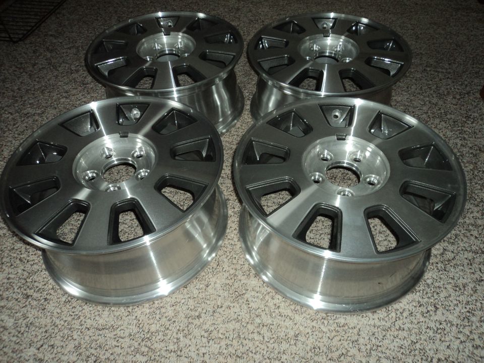 Four silver alloy wheels with black accents on a carpeted floor