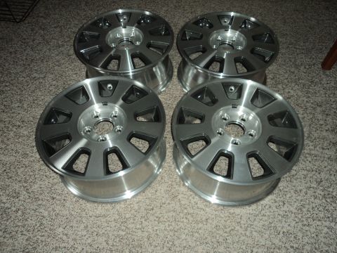 2004 Mercury Grand Marquis - Four silver alloy wheels with dark grey accents are arranged on a carpeted floor. The wheels have a multi-spoke design with cutouts.