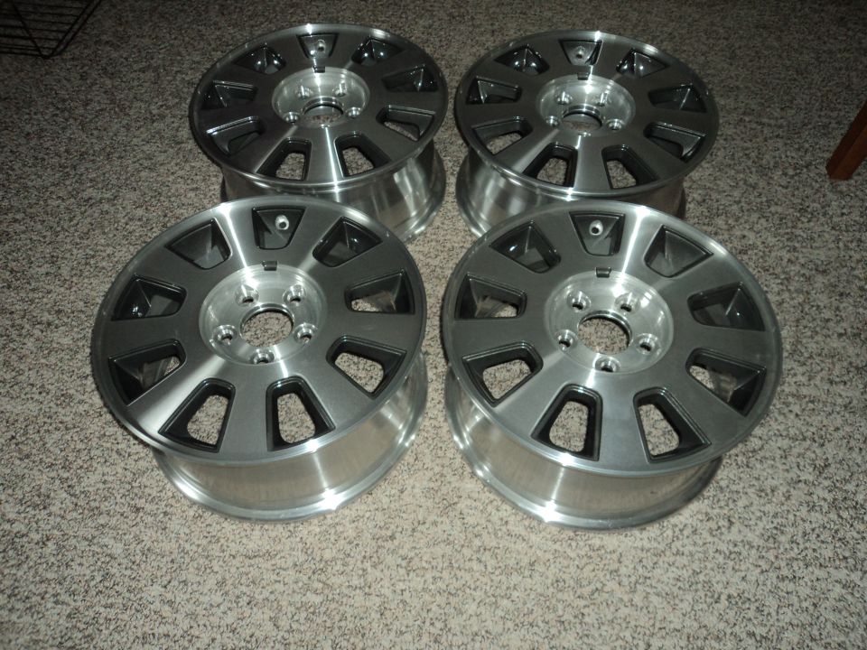 Four silver alloy wheels with dark grey accents on a carpeted floor