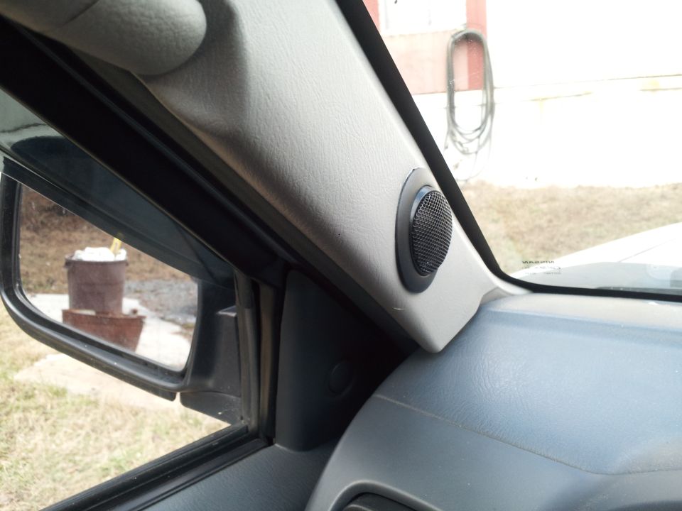Interior view of a vehicle's A-pillar with a speaker, showing the side mirror and an outdoor reflection.