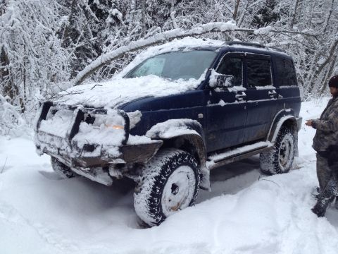 1987 Ford Bronco - This SUV is deep in the snow, surrounded by trees, with a person observing the situation.