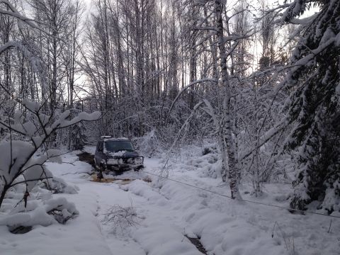 1987 Ford Bronco - A dark SUV is stuck in a snowy forest, with a winch cable attached.