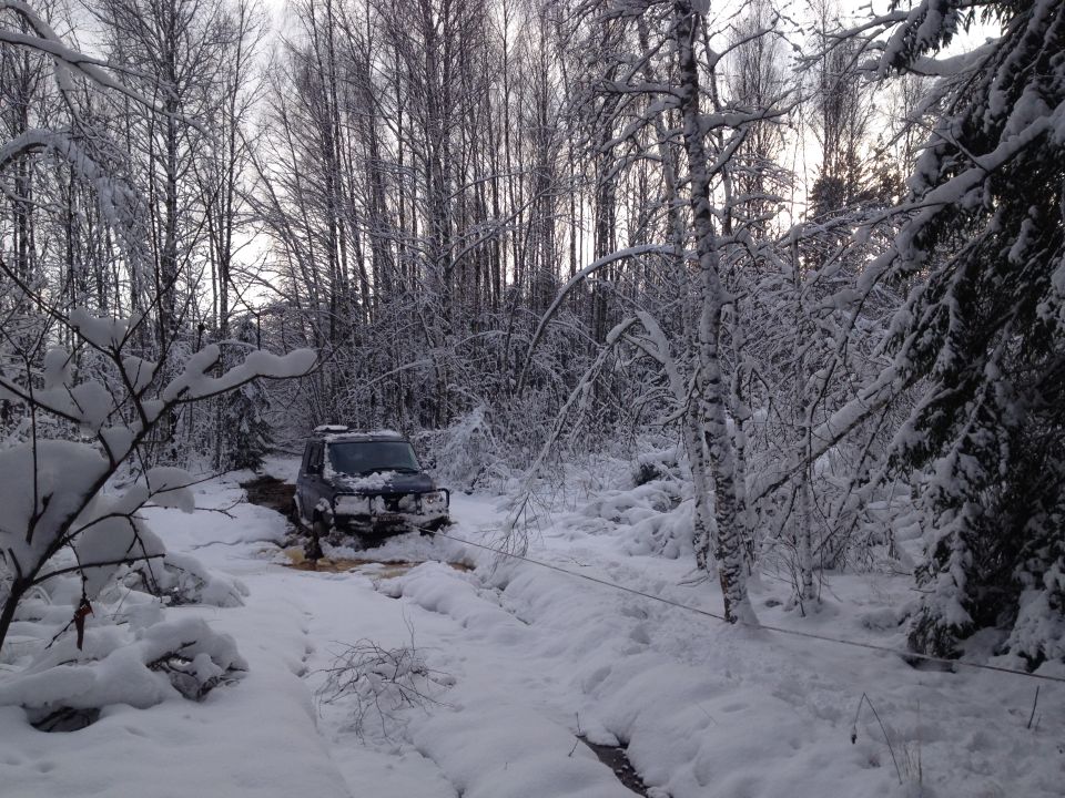 Dark SUV with winch cable stuck in snowy forest path
