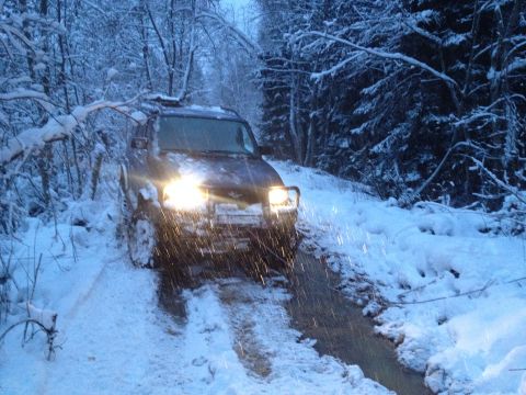 1987 Ford Bronco - A dark colored SUV navigates a snowy, muddy trail surrounded by snow-covered trees.