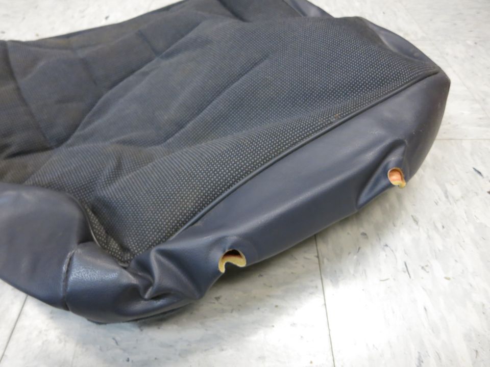 Dark gray car seat cushion with textured fabric and vinyl trim. Shows wear with small holes in the vinyl