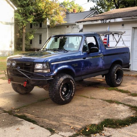 1996 Ford Bronco - A blue 1996 Ford Bronco is parked in a driveway with a garage and houses in the background.