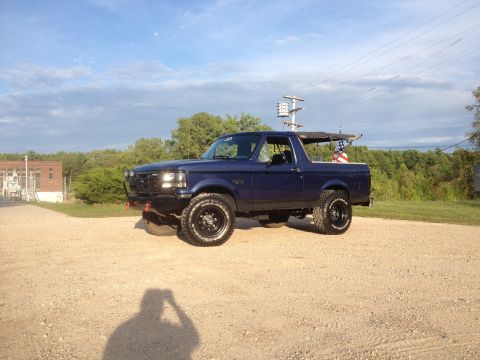 1996 Ford Bronco - Dark blue 1996 Ford Bronco with custom bumper and tires sits parked outdoors.