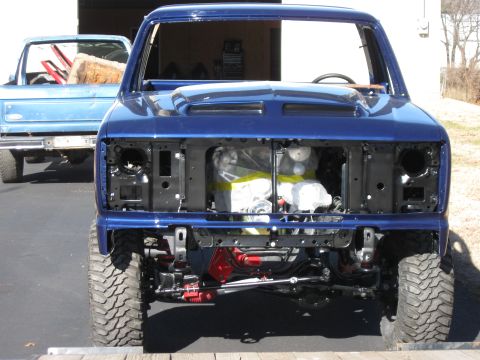 1982 Ford Bronco - The front of a blue Ford Bronco is shown with the grille removed, revealing the engine. A second Bronco is visible in the background.