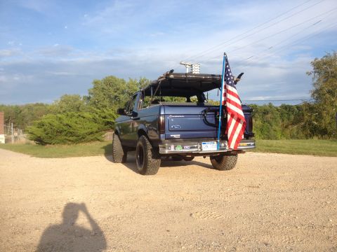 1996 Ford Bronco - A blue Ford Bronco is parked on a gravel surface with trees and a blue sky in the background.
