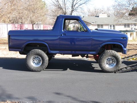1982 Ford Bronco - Side view of a modified blue Ford Bronco, likely from the early 1980s, with large off-road tires.