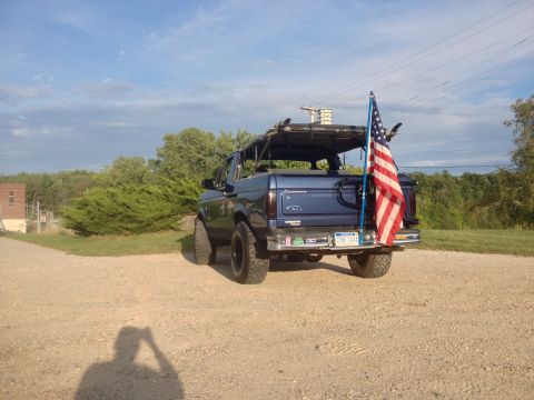 1996 Ford Bronco - This blue 1996 Ford Bronco is seen from the rear, an American flag and a roof rack.