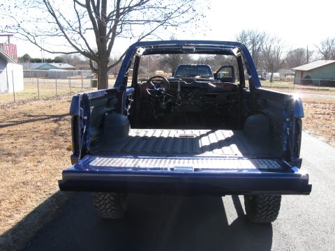 1982 Ford Bronco - Rear view of a stripped-down Ford Bronco, showing the interior and bed. Another vehicle is parked behind it.