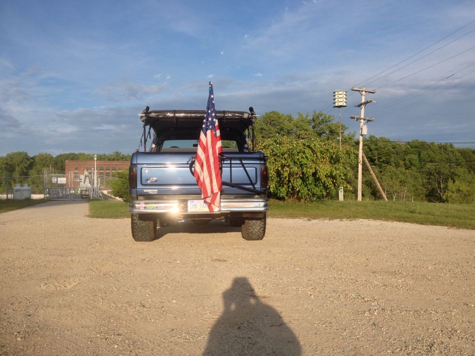 blue SUV with American flag on spare tire mount, parked on gravel lot