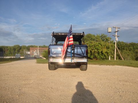 1996 Ford Bronco - A blue SUV is seen from the rear, displaying an American flag on its spare tire mount.