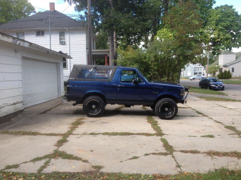 1996 Ford Bronco - A blue Ford Bronco sits in a driveway on a cloudy day, with a house and trees in the background.