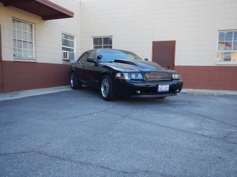 2003 Ford Crown Victoria - Photo of a black Mercury sedan with halo headlights parked outside a building, not a technical document.