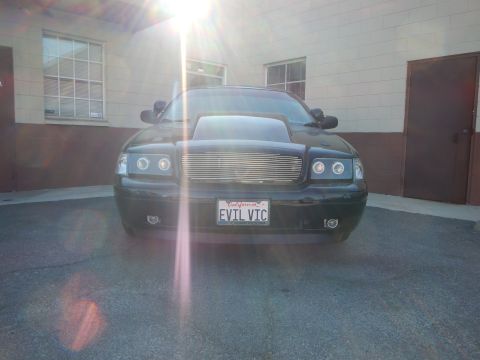 2003 Ford Crown Victoria - Head-on view of a black Ford Crown Victoria with halo headlights and a California EVIL VIC license plate, sun flare above.