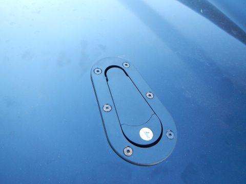 2003 Ford Crown Victoria - Close-up of a black oval hood-pin latch plate mounted on a glossy blue automotive body panel.