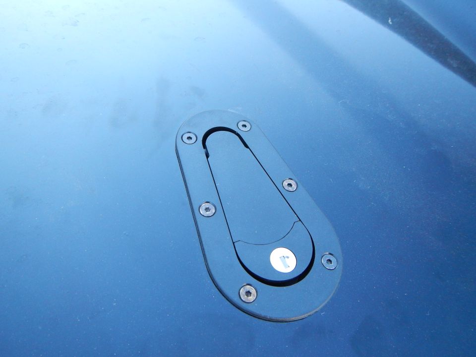 Close-up of black hood pin latch mounted on blue car body panel