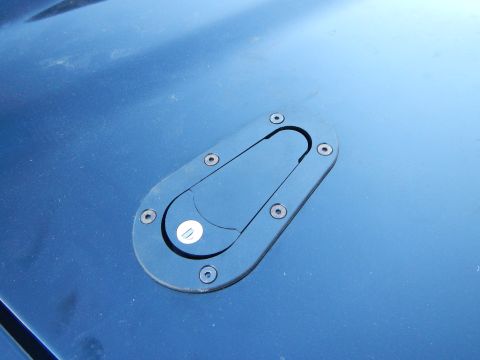 2003 Ford Crown Victoria - Photo of an aftermarket flip-style fuel filler door on a blue car body panel, not a technical document.