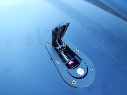 2003 Ford Crown Victoria - Close-up of an open hood-pin latch revealing its hinged arm and spring mechanism on a blue body panel.