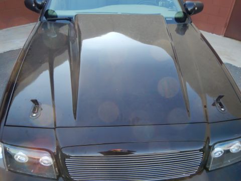 2003 Ford Crown Victoria - View down the raised cowl hood of a black Ford Crown Victoria toward its chrome billet grille and halo headlights.
