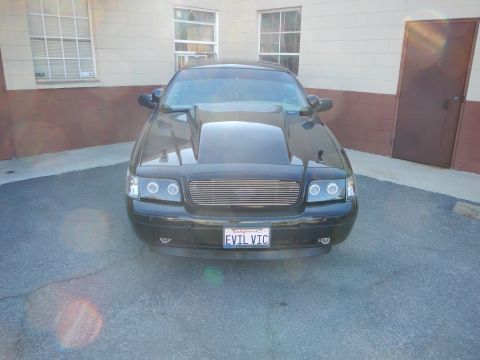 2003 Ford Crown Victoria - Head-on view of a black Ford Crown Victoria with a raised cowl hood, billet grille, and California EVIL VIC plate.