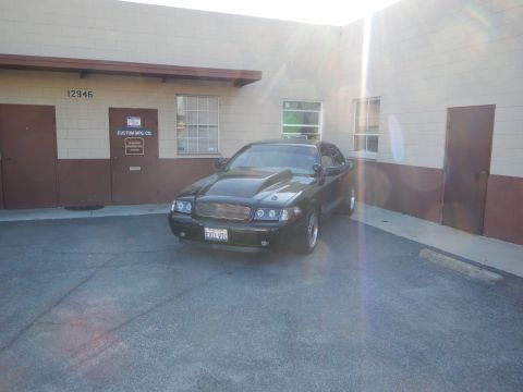 2003 Ford Crown Victoria - Front-right view of a black full-size sedan parked diagonally beside a commercial building numbered 12946.