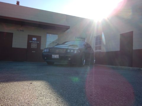 2003 Ford Crown Victoria - Front three-quarter view of a black sedan parked outside a building, with intense sunlight and lens flare across the frame.