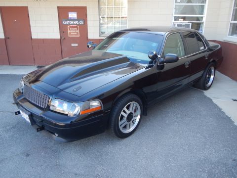 2003 Ford Crown Victoria - Close front view of a black sedan showing its cowl-induction hood, chrome grille and chrome-lipped wheels.