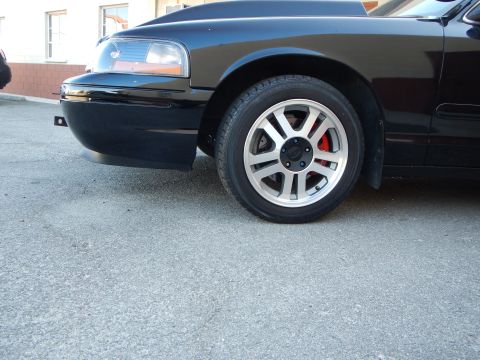 2003 Ford Crown Victoria - Detail of a black sedan's front wheel, a silver multi-spoke alloy with a red brake caliper and low-profile tire.