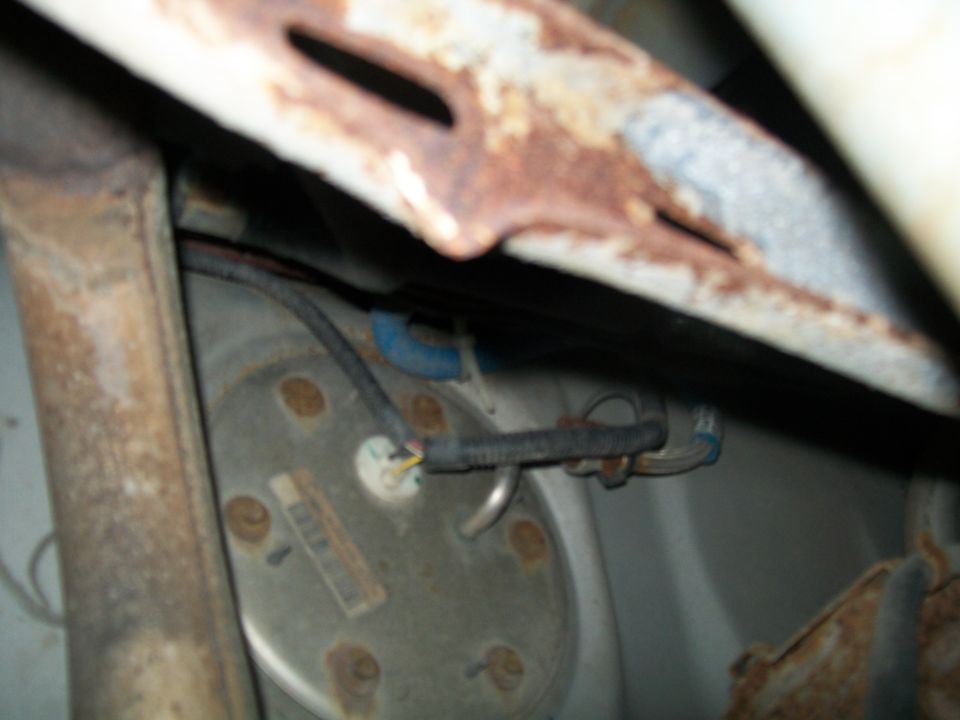 Close-up of a vehicle's fuel pump assembly with rusty metal components and wiring