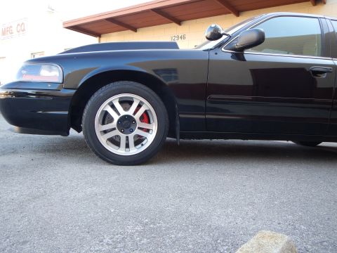 2003 Ford Crown Victoria - Side profile of a black sedan's front fender and silver alloy wheel with a red brake caliper.