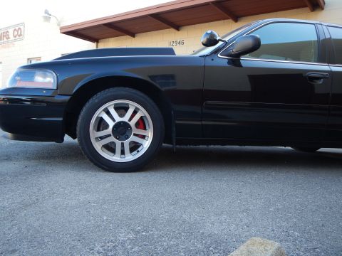 2003 Ford Crown Victoria - Low-angle shot of a black sedan's front silver wheel and red caliper, parked under a building awning.