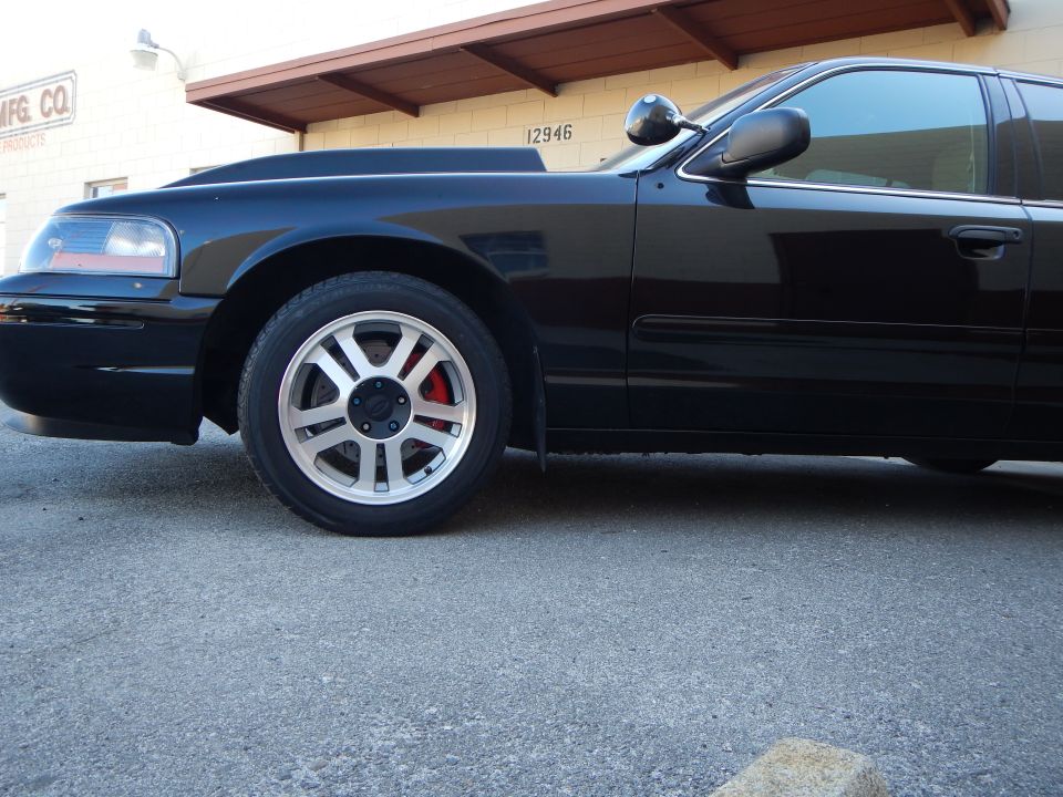 Front wheel of black sedan under a building awning, red caliper visible
