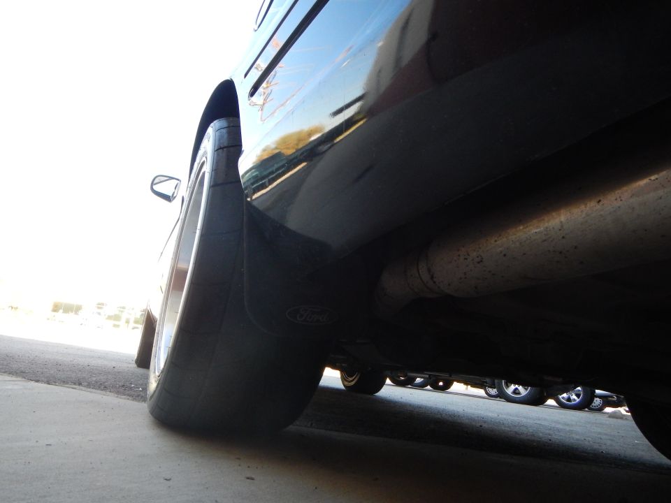 Underside view of black sedan rear wheel with Ford mud flap and exhaust