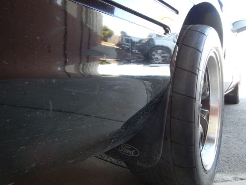2003 Ford Crown Victoria - Close low-angle view of a black sedan's rear wheel and a Ford-logo mud flap above the pavement.
